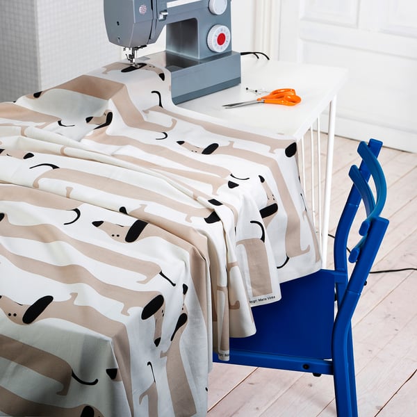 Blue sewing chair with white fabric printed with cartoon dogs draped over it, next to a grey sewing machine.