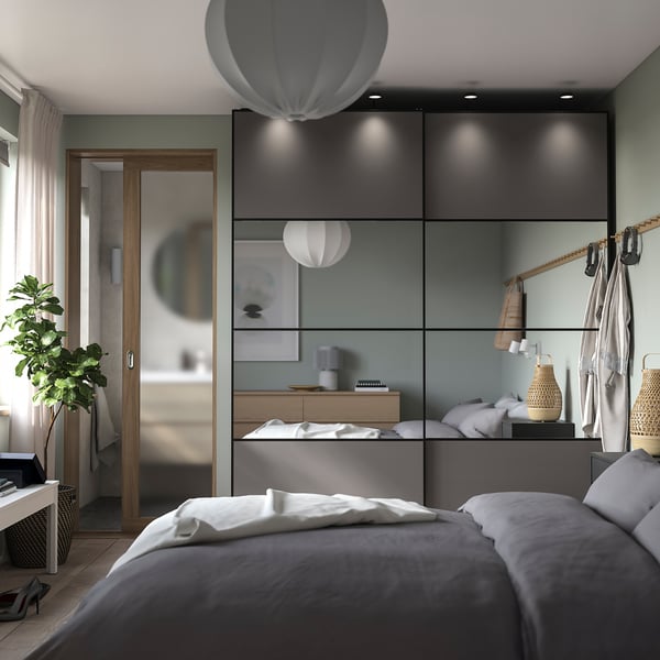Modern bedroom with minimalist decor: grey bed, wood furniture, unique lamps, and mirrored sliding door to bathroom.