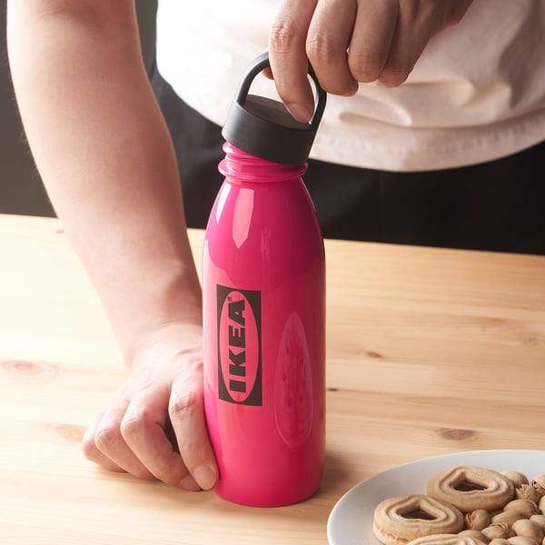 A person holding a pink ikea bottle, showcasing its loop handle on the lid, ready to carry.