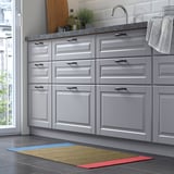 Modern kitchen with grey cabinets, marble counter, and colourful striped yellow, blue, red rug.