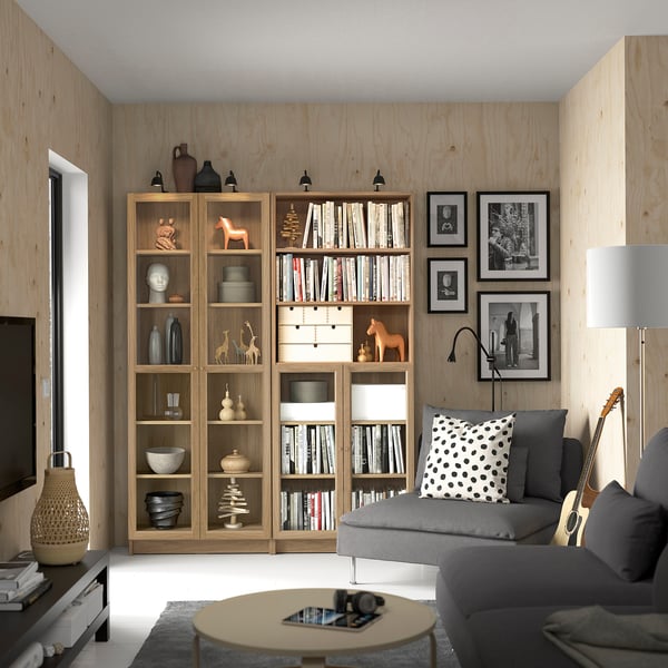 Living room with wooden BILLY bookcases, grey sofa, and framed photos. Bookcases filled with books, decor items. Tv on the left.