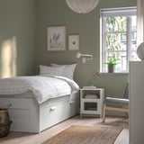 Compact bed frame with storage, sleek & white, ideal for small spaces. Two drawers, positioned against green wall with decor.