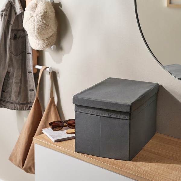 Grey box lid on shelf, with notebook and sunglasses. Coat and bag hang in background.