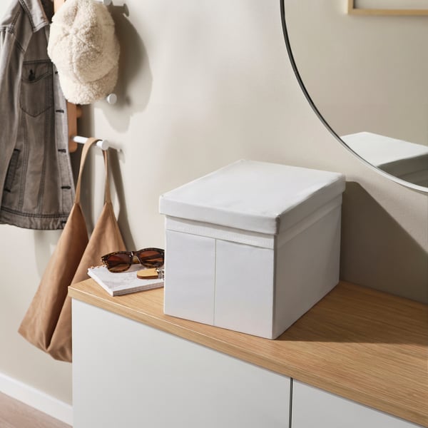 Grey lid on white box, beside bag, sunglasses, book, and mirror.