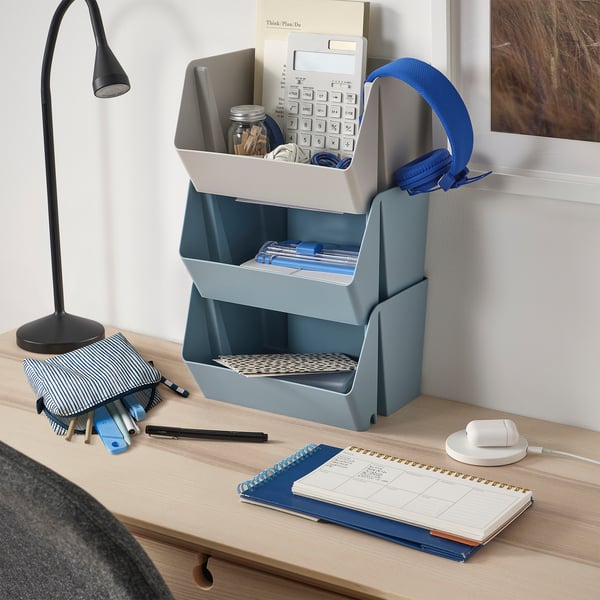 Blue EKAÅN headphone case on desk with office supplies. Holds headphones, calculator, and other items. Made of recycled polyester.