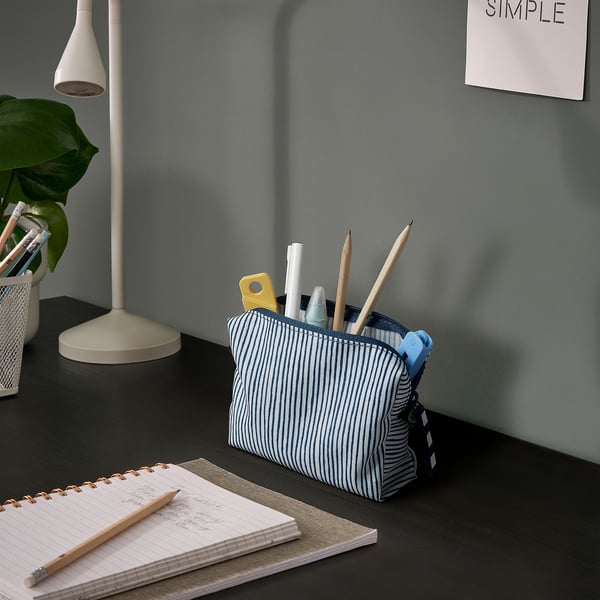 A stylish blue and white striped pouch holds stationery items like pencils, pens, and markers, placed on a dark desk.