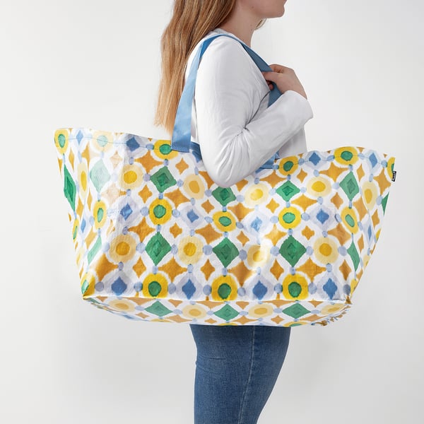 Person holding large patterned tote bag, ideal for shopping or storage. Bold colours, durable, and reusable.
