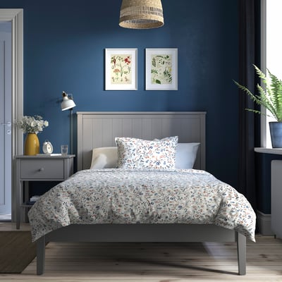 Blue bedroom with floral bedding, grey bed, bedside table, lamp, art, fern.