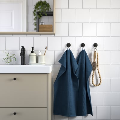 Modern bathroom with dark blue GULLDYNA towels, black faucets, white containers, and plant.