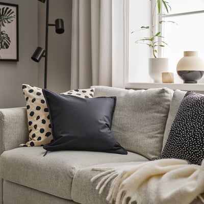 Modern living room with beige sofa, black & white pillows, GURLI cushion, blanket, lamp, and plant.
