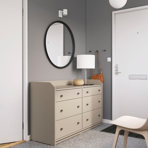 Modern entryway with HAUGA chest, white lamp, round mirror, and brown purse on a creamy dresser.
