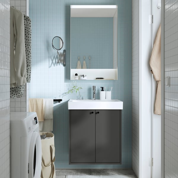 Small, modern bathroom with light blue tiles. Dark grey HAVBÄCK cabinet, white sink, mirror, and laundry basket. Towels hang beside a washing machine.