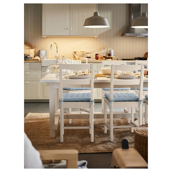 Kitchen with white cabinets, island, pendant lights, and chairs with blue cushions.