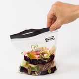 Hand opens colourful, reusable IKEA ISTAD bag for food or small items, made from 50% renewables.