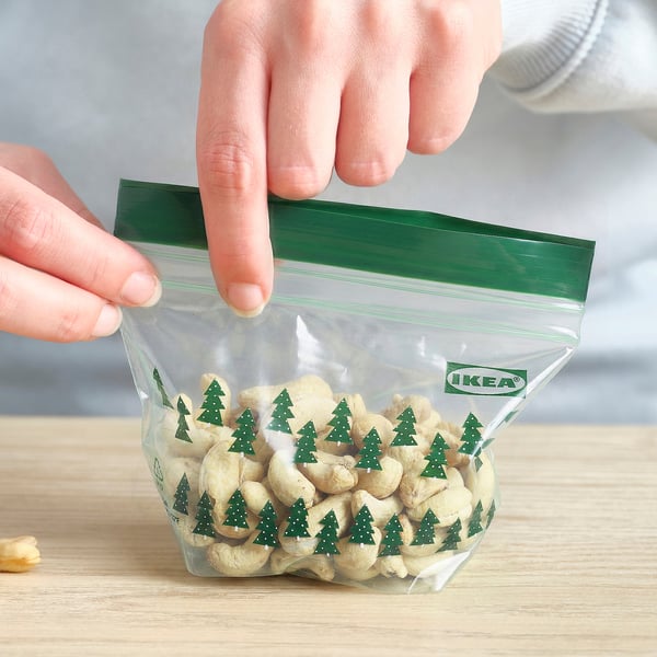 A hand seals a green IKEA ISTAD bag filled with cashews, showing a christmas tree pattern and resealable top.