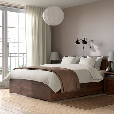 Modern bedroom KRANSSALVIA brown bedding on wooden bed, large window with curtains, and hanging lamps. Light-colored rug and lamps on nightstands.