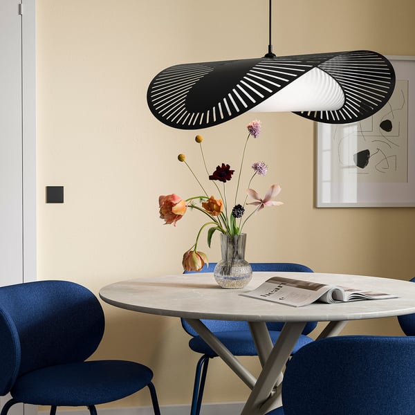 A modern dining area with a KVÄLLSDOPP lamp in black, casting warm light over a marble table and blue chairs.