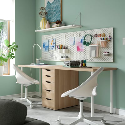Modern home office with wooden desk, two chairs, pegboard, and decor.