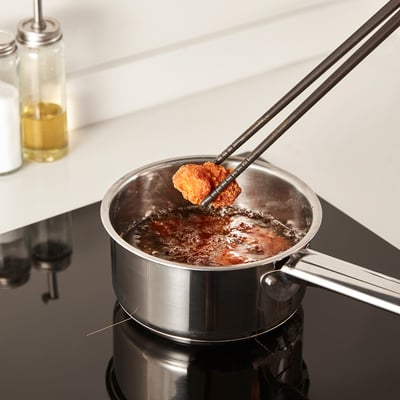 Chopsticks with silicone tips grip fried food safely over boiling pot.