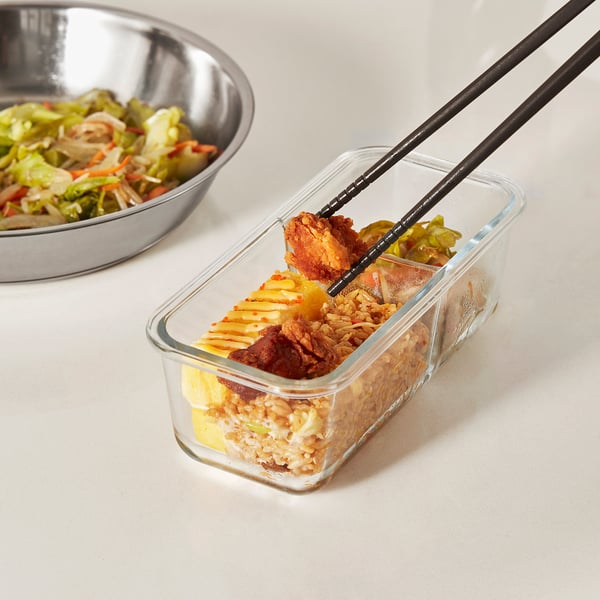 Chopsticks with spoon ends holding food from glass container, showcasing cooking assistance.