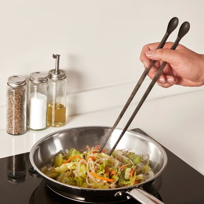 Hand stir-fries veggies in pan using LUNGROT, showing its cooking and tasting utility.