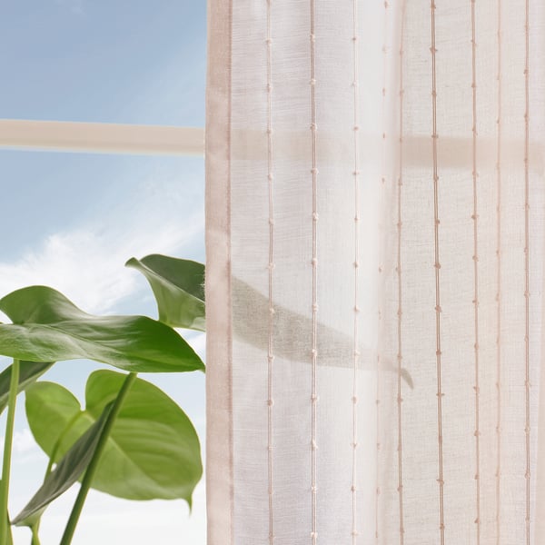 A pale curtain with small dots and green plant leaves partially covers a window, allowing soft light to philtre through.