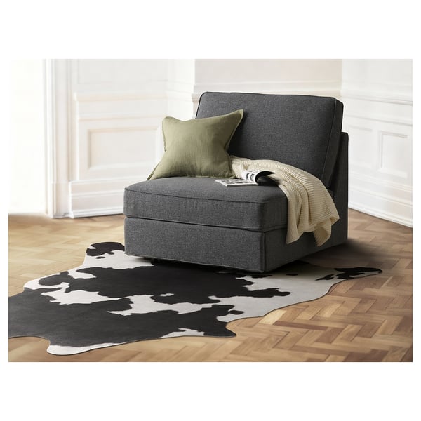 MAXTAXA cowhide-style rug in black and white on wooden floor with grey chair and green pillow nearby.