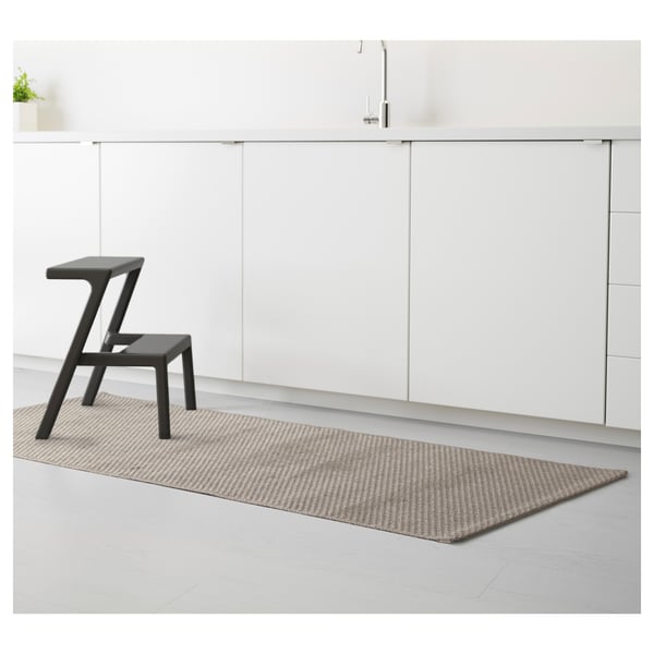 Minimalist kitchen modern, black stool atop patterned rug. White cabinets and sleek tap enhance clean, elegant design.