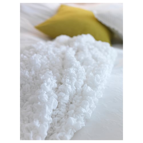 White, fluffy blanket on bed, yellow pillow, textured, cosy, recycled material.