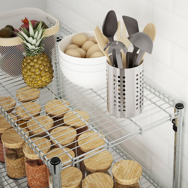 Metal wire shelf holding containers, pineapple, kitchen tools, and jars with wooden lids. Neatly organises kitchen items.