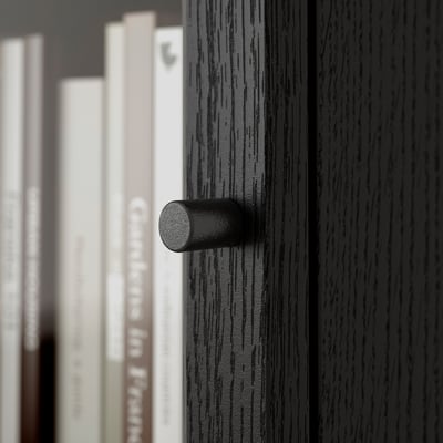 Black handle on dark wooden drawer, with blurred bookshelf in background.