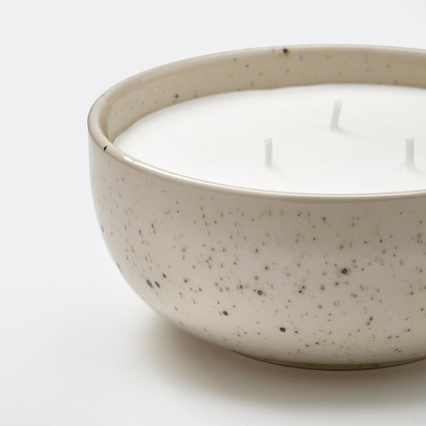 Close-up of elegant white speckled stoneware candle with three wicks, emitting a warm, inviting atmosphere.