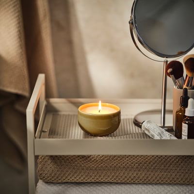 Lit PÄRLHÖNA candle on tray beside makeup mirror.