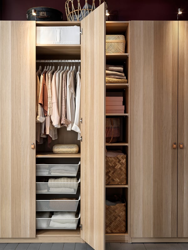 Wooden PAX closet organised with clothes, baskets, and drawers, open showing storage solutions.