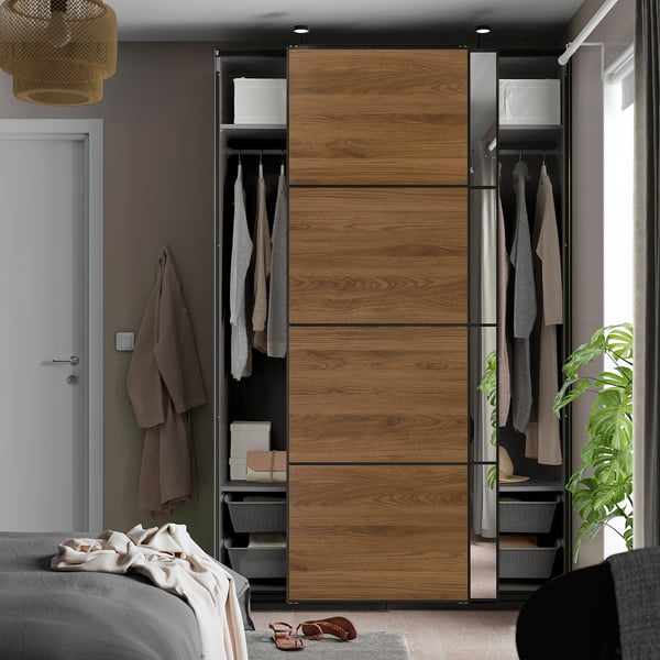 Modern bedroom with PAX wardrobe featuring sliding wooden doors, mirrored section, hanging clothes, shelves, and overhead lighting.