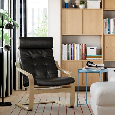 Modern living room with black POÄNG armchair, light blue side table, bookshelf, plant, and striped rug.