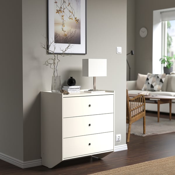 White RACKNÄS chest with 3 drawers, vase, and lamp in living space.