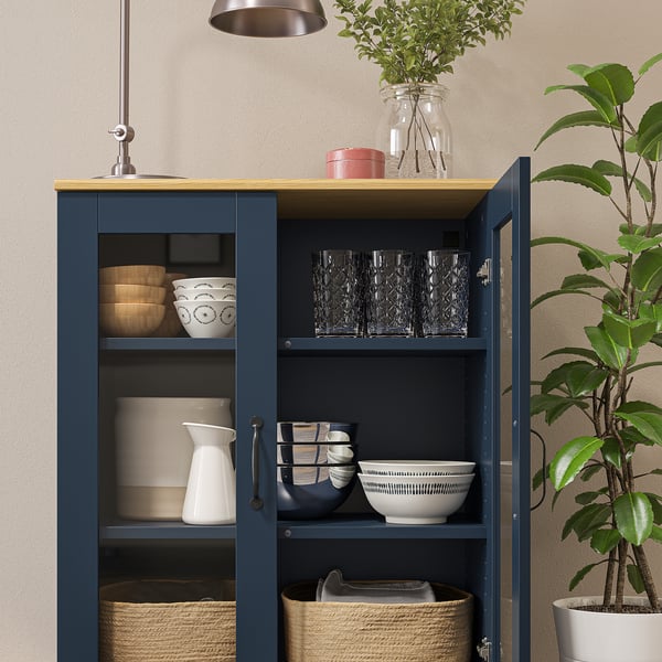 Glass-door cabinet with wooden top, displaying items, adjustable shelves, houseplant.