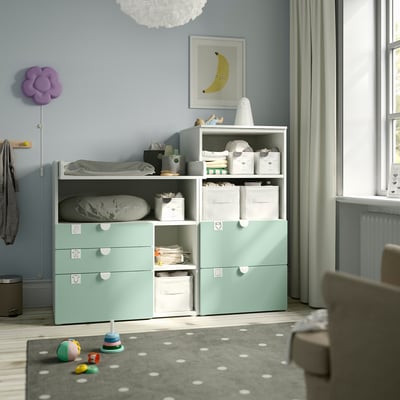 Kids room with mint green storage, toys, changing table, blue walls, window light.