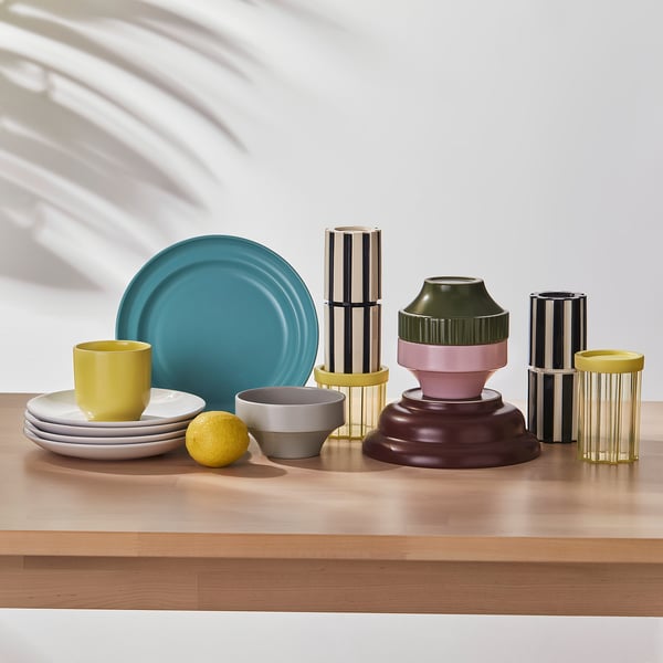 Assorted colourful ceramic tableware on wood shelf, including plates, cups, and vases with unique designs and textured edges.
