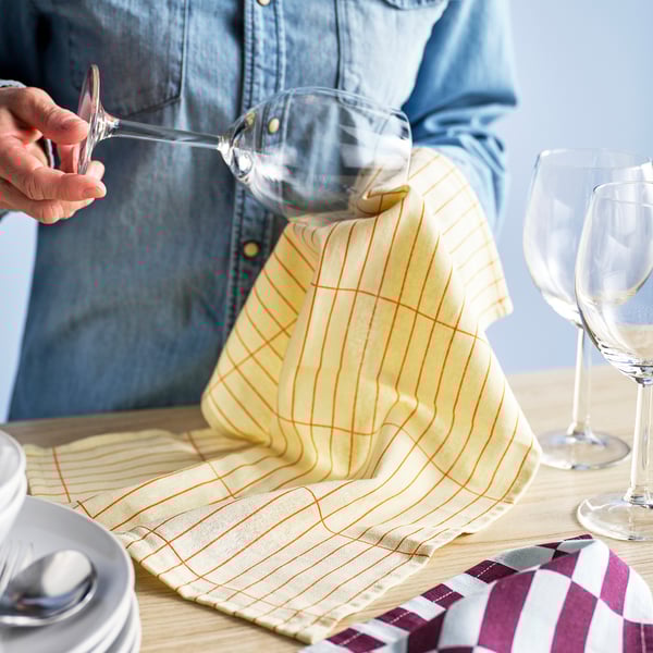 Person pours liquid into glass on table with colourful towels.