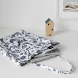 A blue fabric laptop case with floral patterns lying on a white surface next to a wooden birdhouse.