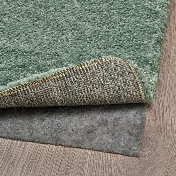 A green low-pile rug placed on a dark grey rug underlay, showcasing its anti-slip function.