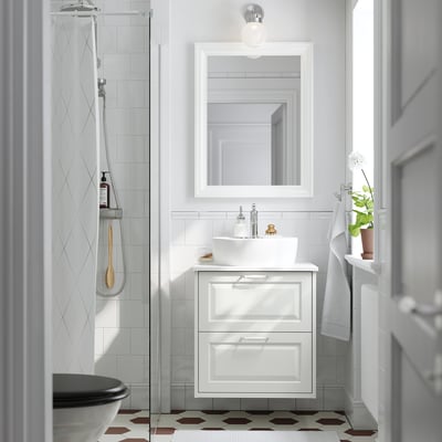 White bathroom with TÄNNFORSEN vanity, sink & mirror. Round sink, large vanity, partial shower, small plant & towel.