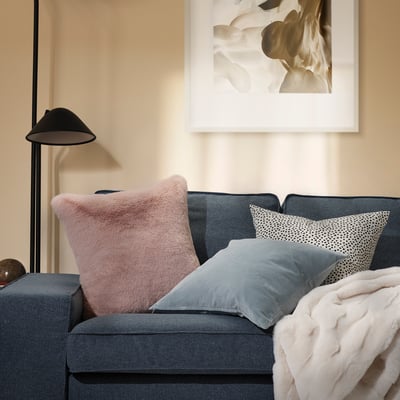 Living room with pink faux fur cushions on grey sofa, lamp, and abstract art.