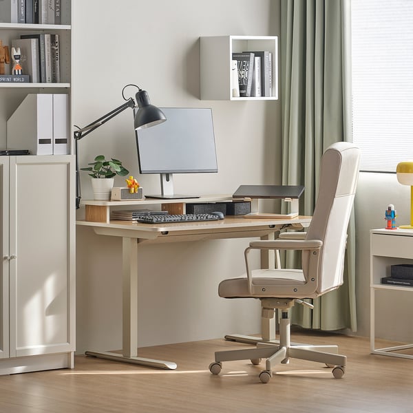 Home office setup with sit-stand desk, chair, lamp, plant, monitor, bookshelf, and window.
