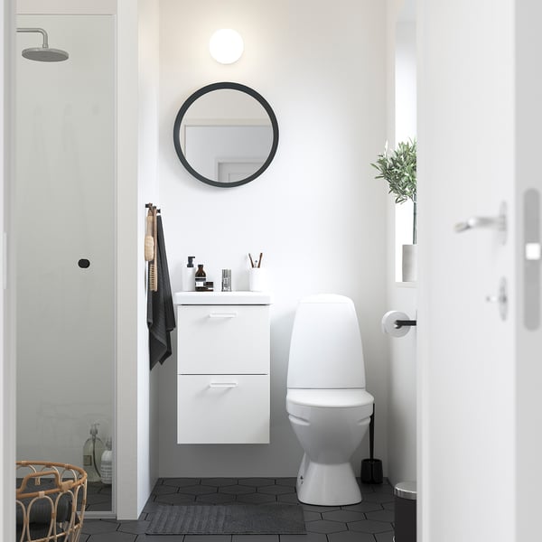 Modern minimalist bathroom: white toilet beside white cabinet, round mirror above, black accents, and grey tiled floor.