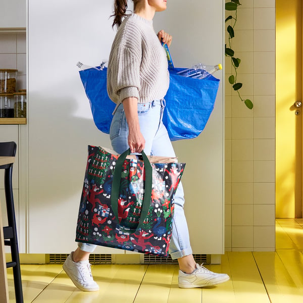 Person carrying large colourful bag near yellow door. Bag named VINTERFINT with vibrant pattern.