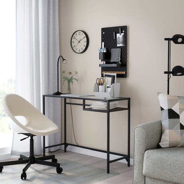 Black vittsjjo laptop table with glass top, chair, sofa, and striped pillows.