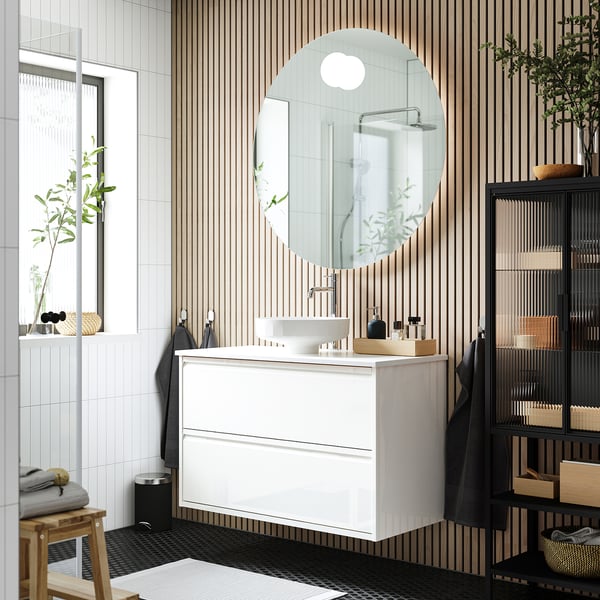 A modern bathroom featuring ÄNGSJÖN vanity, round mirror, black shelves, vessel sink, and wooden accents.